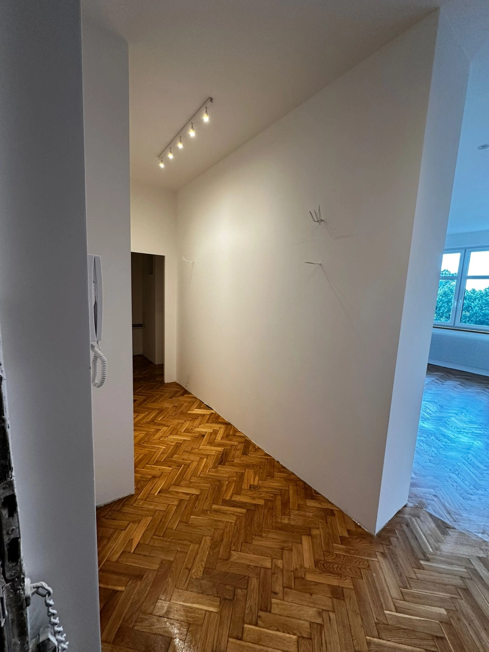 Korytarz z ułożonym parkietem w jodełkę, białe ściany i oświetlenie punktowe, usługa Układanie podłóg